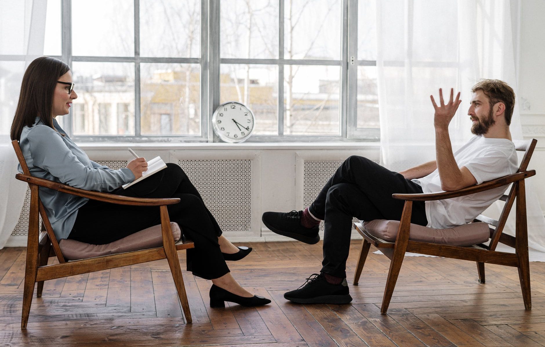 person in black pants and black shoes sitting on brown wooden chair